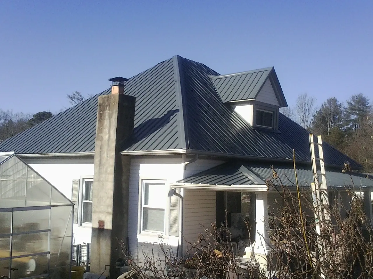 Dark blue standing seam metal roof on a white farmhouse with dormer — Slate & Tile Roof Repair by Roofing Brothers in Saint Joseph
