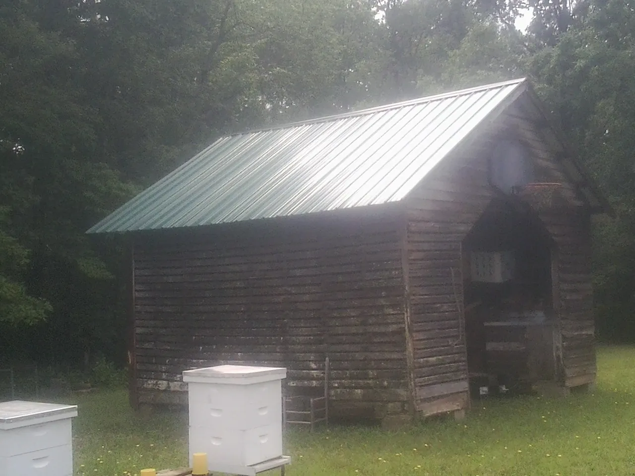 Green metal roof on a weathered barn beside stacked beehives in Saint Joseph